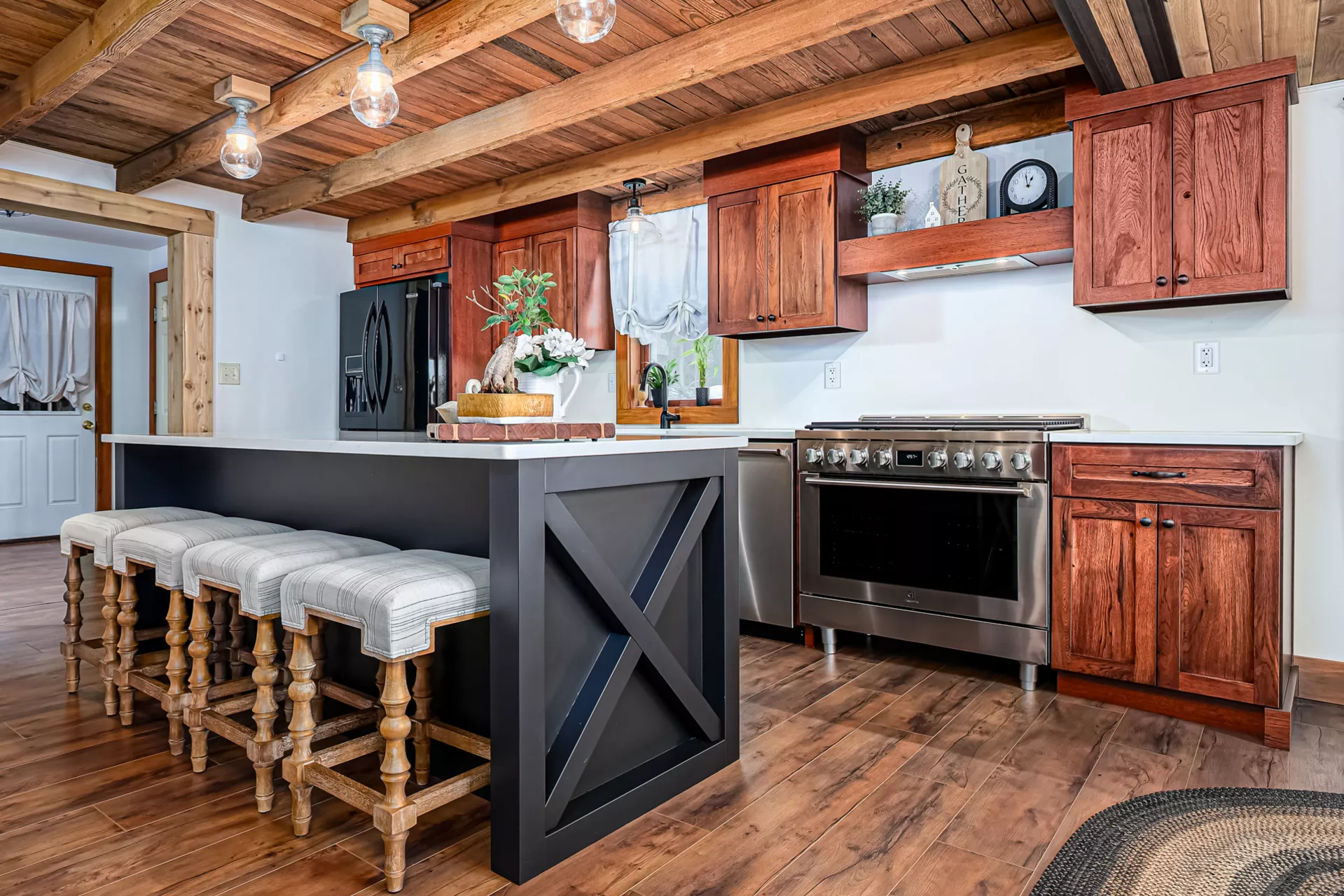 Noah F. Boyle Cabinets Elizabethtown, PA Rustic kitchen with wood-beamed ceiling, dark wood cabinets, stainless steel appliances, an island with stools, and decorative items on open shelves.