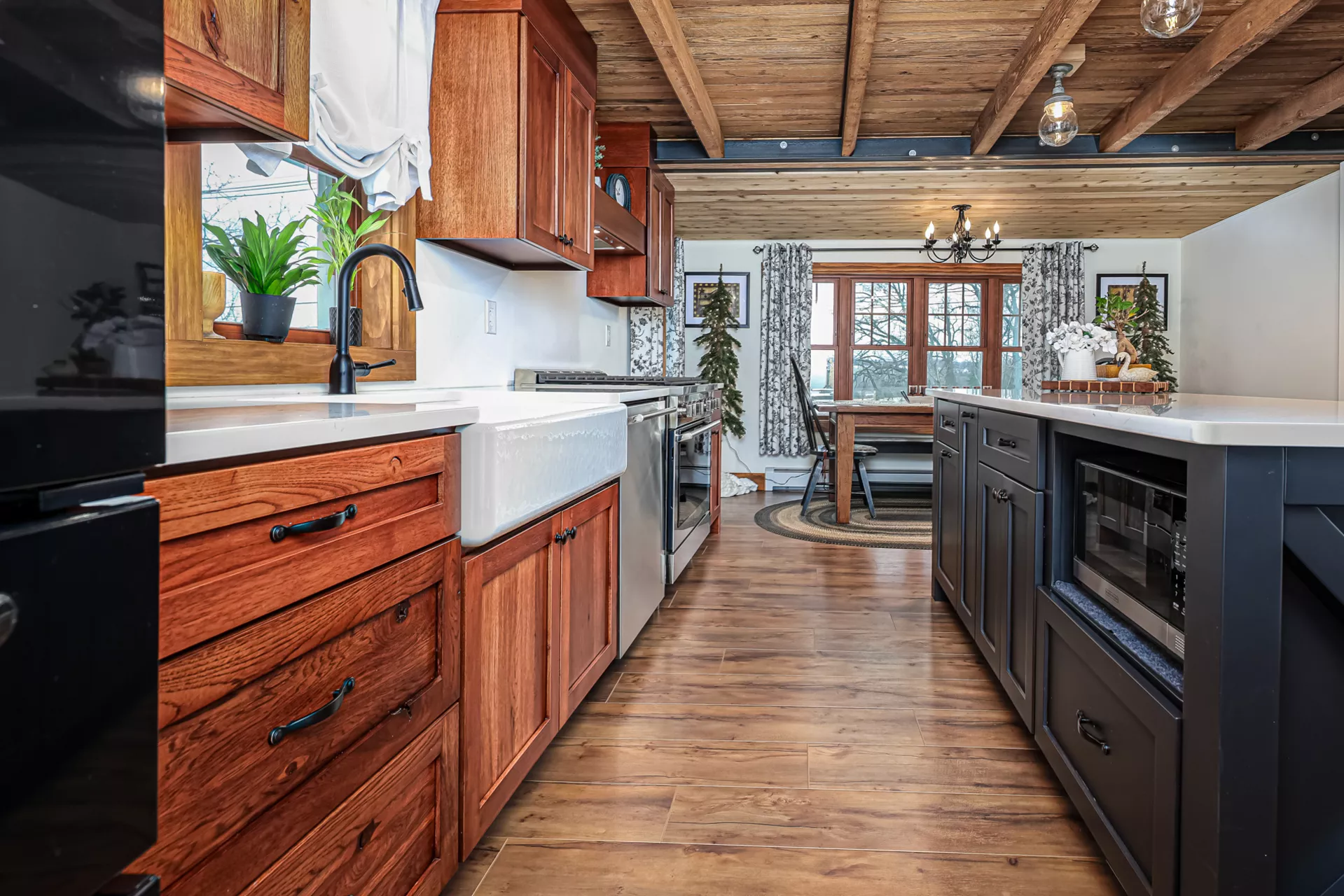 Noah F. Boyle Cabinets Elizabethtown, PA A modern kitchen with wood cabinets, stainless steel appliances, white countertops, and a view of a dining area with large windows and wood accents.