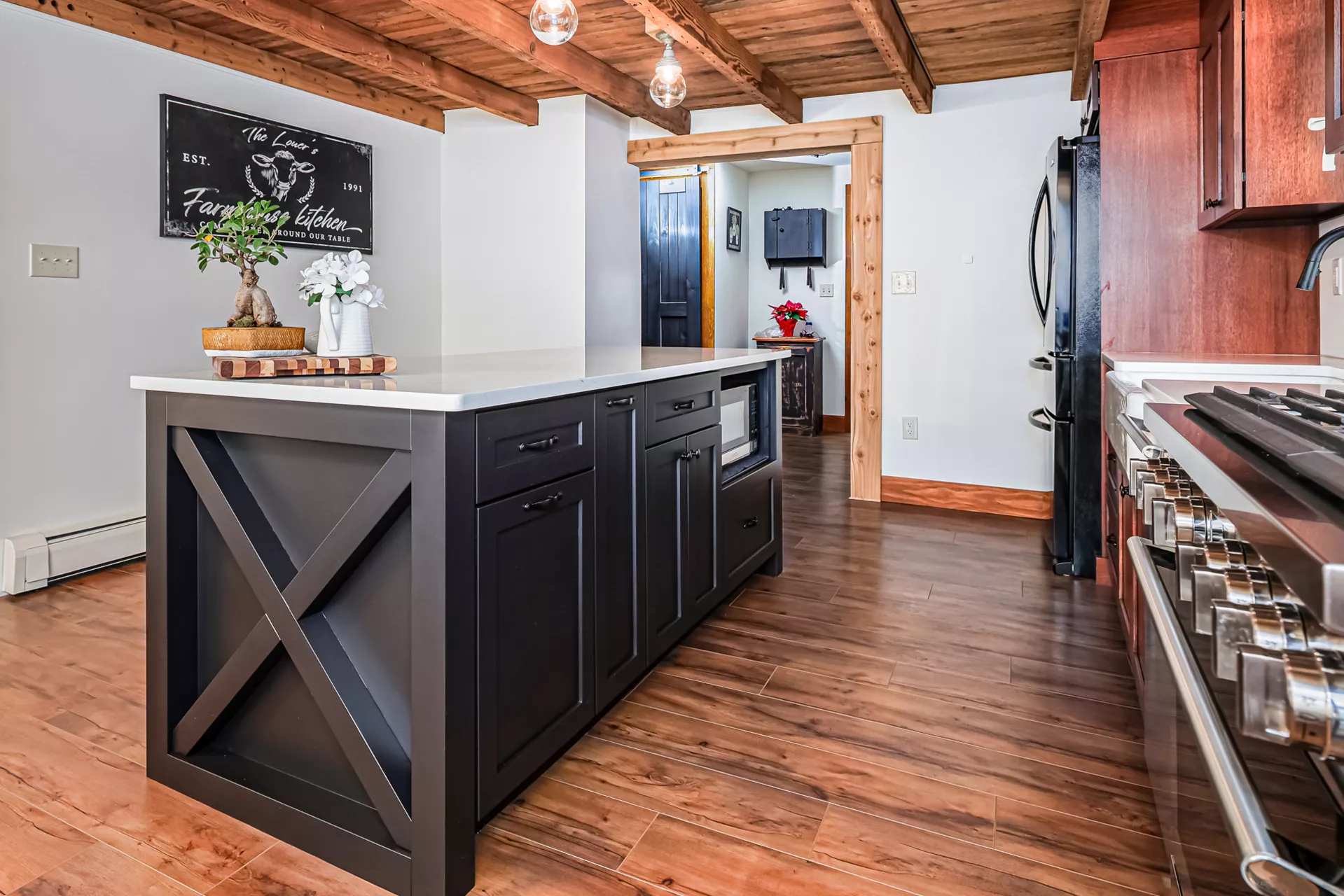 Noah F. Boyle Cabinets Elizabethtown, PA Modern kitchen with a wooden floor, black island with drawers, white countertop, gas stove, wooden ceiling, and wall decor.