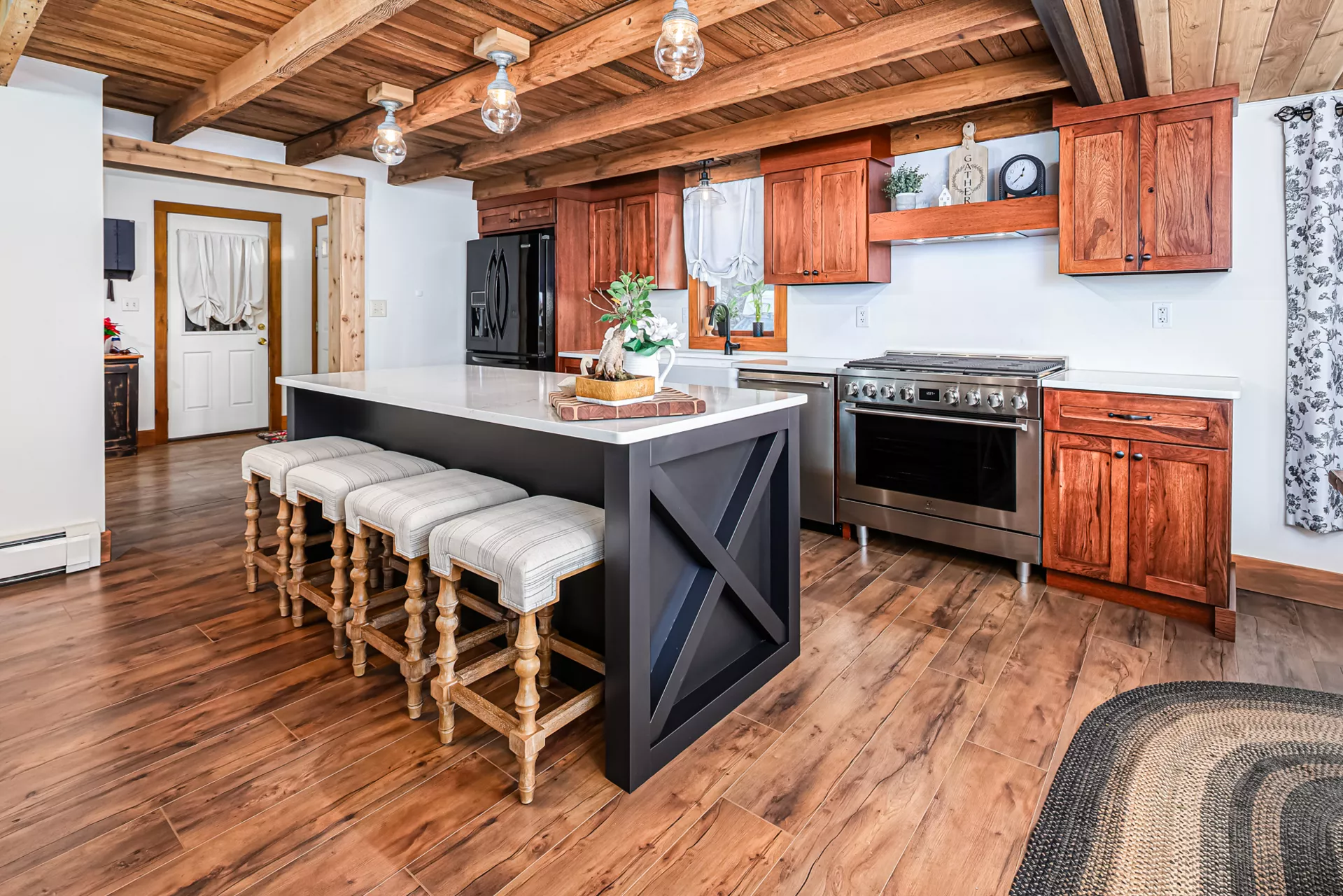 Noah F. Boyle Cabinets Elizabethtown, PA A rustic kitchen with wood cabinets, exposed beams, a large island with four cushioned stools, hardwood floors, and stainless steel appliances.