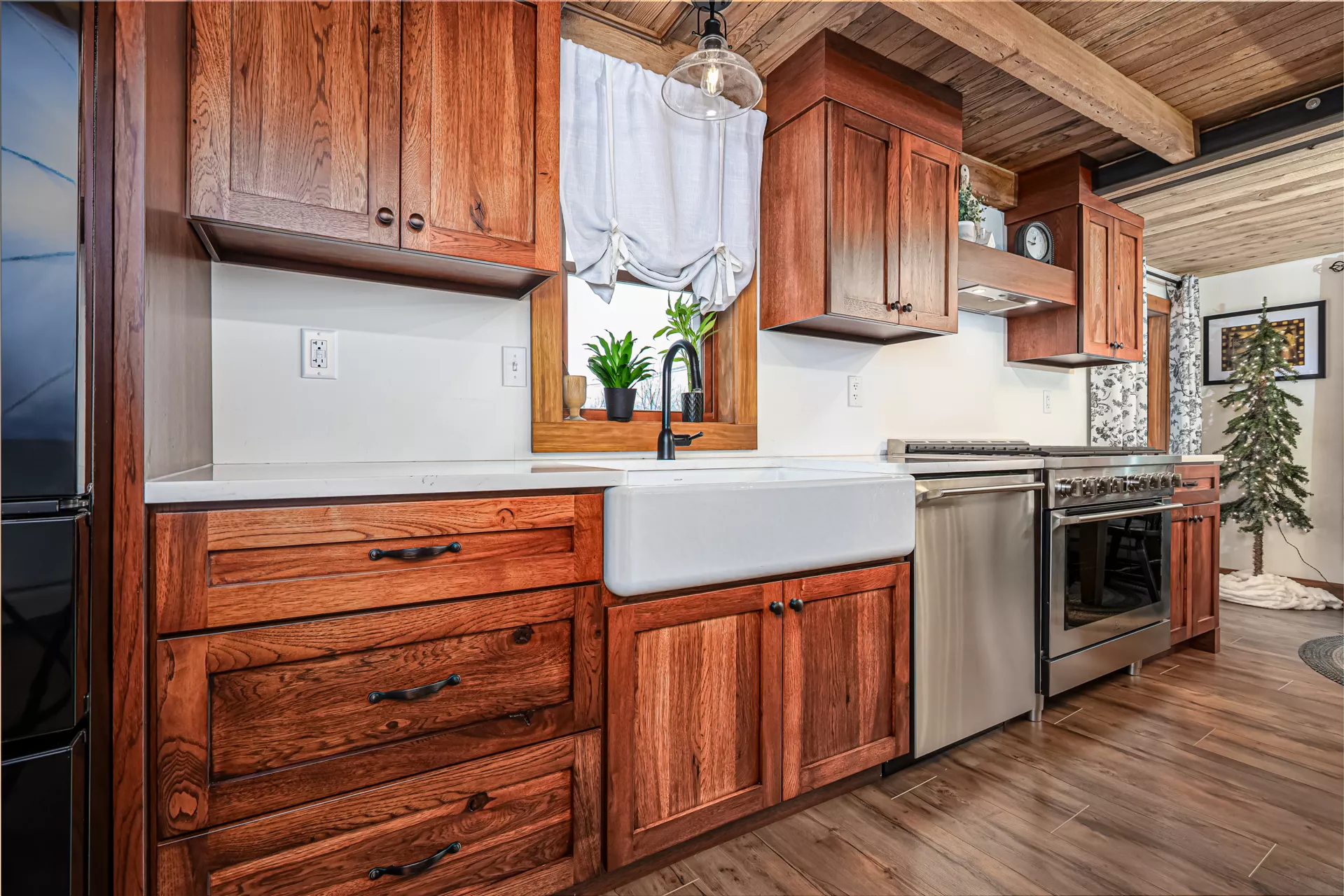 Noah F. Boyle Cabinets Elizabethtown, PA Rustic kitchen with wood cabinets, farmhouse sink, stainless steel appliances, white backsplash, and potted plants on the window ledge.